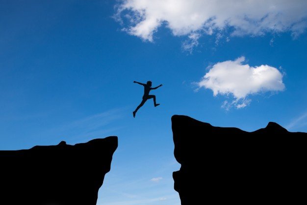 Free Photo | Man jump through the gap between hill.man jumping over cliff on sunset background,business concept idea