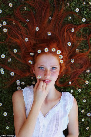 Red haired girl with freckles wearing a white dress with flowers in her hair and blue eyes