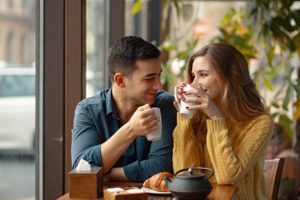 Young attractive couple on date in coffee shop having a conversation and enjoying the time spent with each other. — woman, mug - Stock Photo | #224437972
