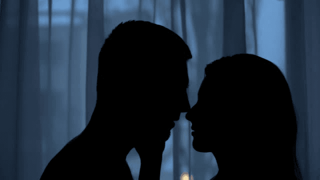 Couple shadow tenderly kissing in twilight room, nightlife intimacy, feelings