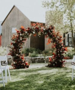 a lush dark autumn wedding arch with red leaves and blooms, white roses and much greenery – HappyWedd.com