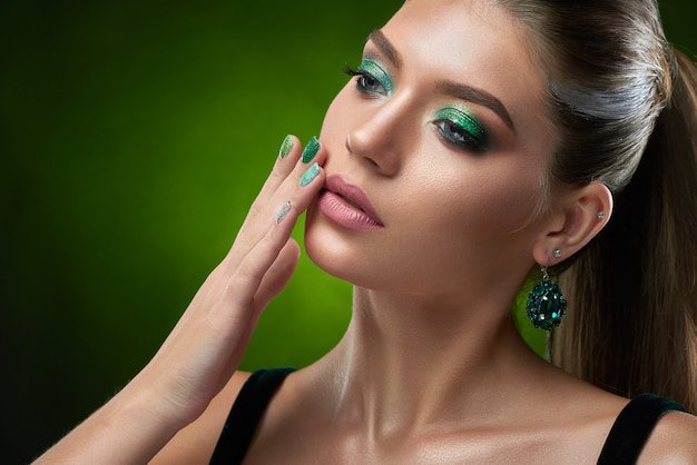 Premium Photo | Portrait of sensual beautiful woman with shiny green makeup touching perfect bronze skin of face and plump lips. brunette woman wearing in black top, big rounded earring posing .